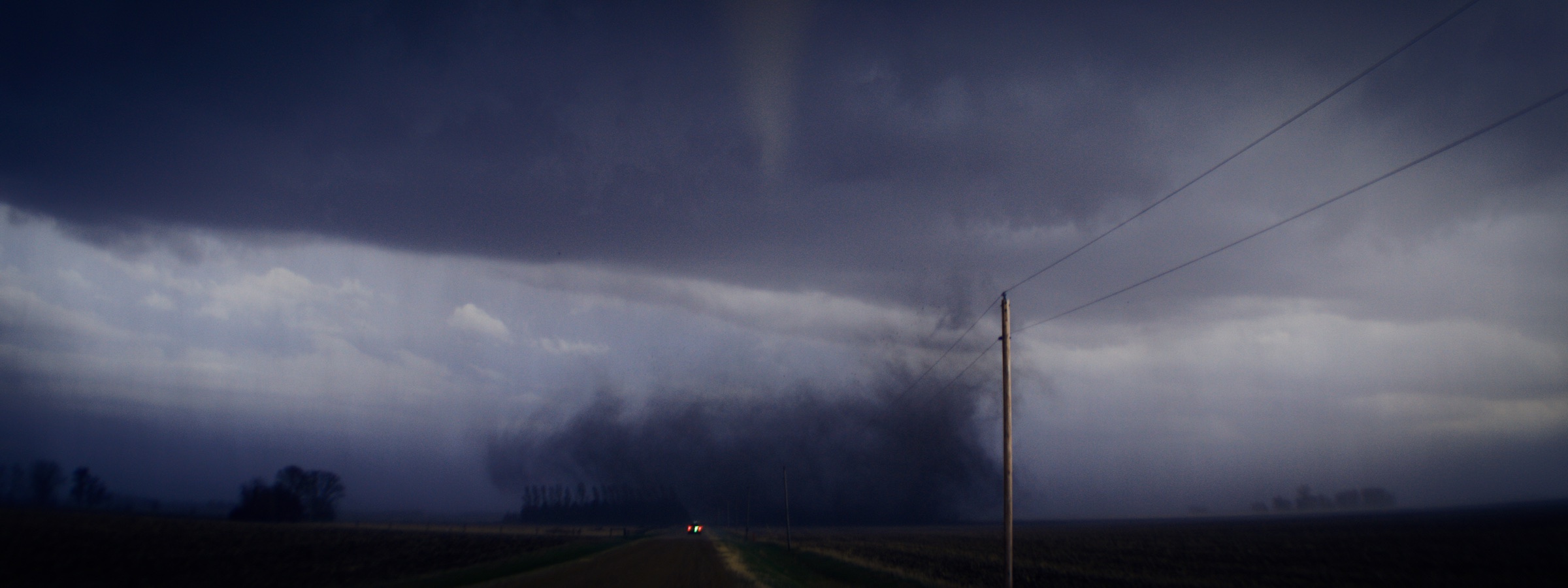 Large tornado under a dark storm base near a rural road